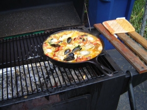 Grilling paella over a wood fire on a charcoal grill